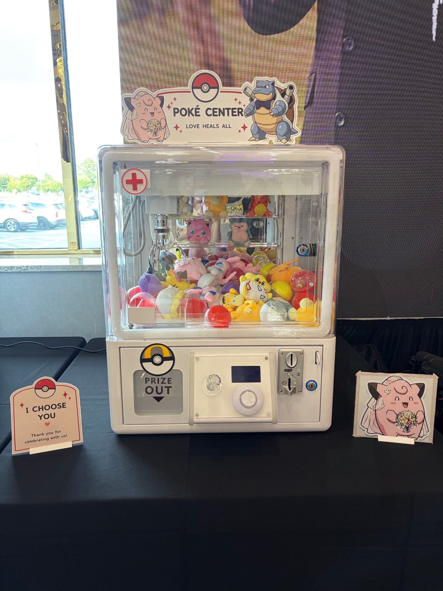 Claw machine with a custom pink 'Poké Center' topper sign and themed table cards